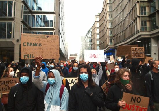 A crowd of people protesting against racism at a Black Lives Matter march. The people are wearing masks and holding cardboard signs