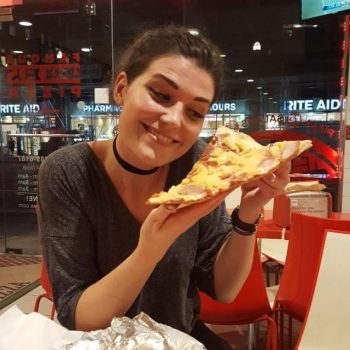 A woman smiling holding a slice of pizza