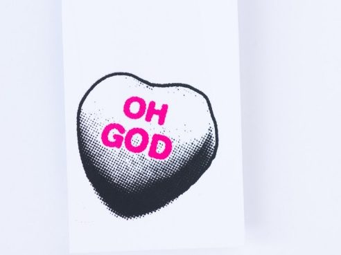 An image of a white card with a graphic illustration of a chocolate heart with the words OH GOD written in pink on it.
