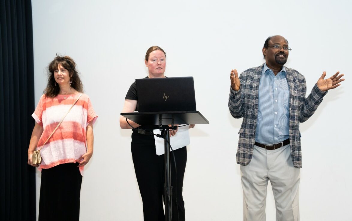 Three people stood on a stage with a laptop, presenting