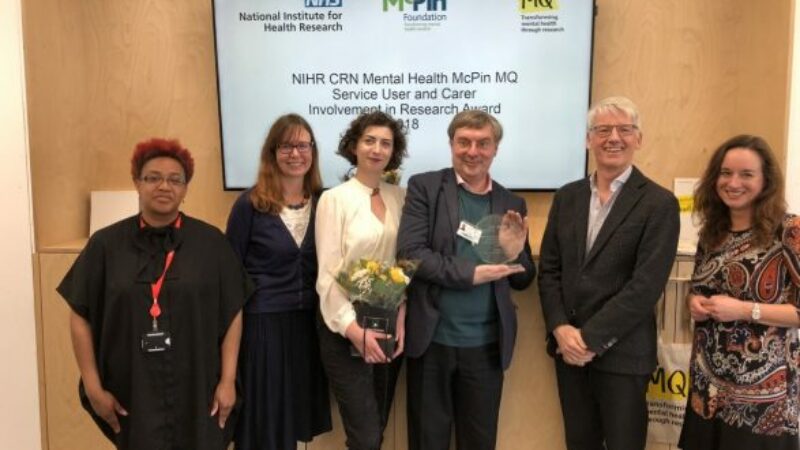 A group of people in front of a screen which reads 'NIHR CRN Mental Health McPin MQ Service User and Carer Involvement in Research Award 208'