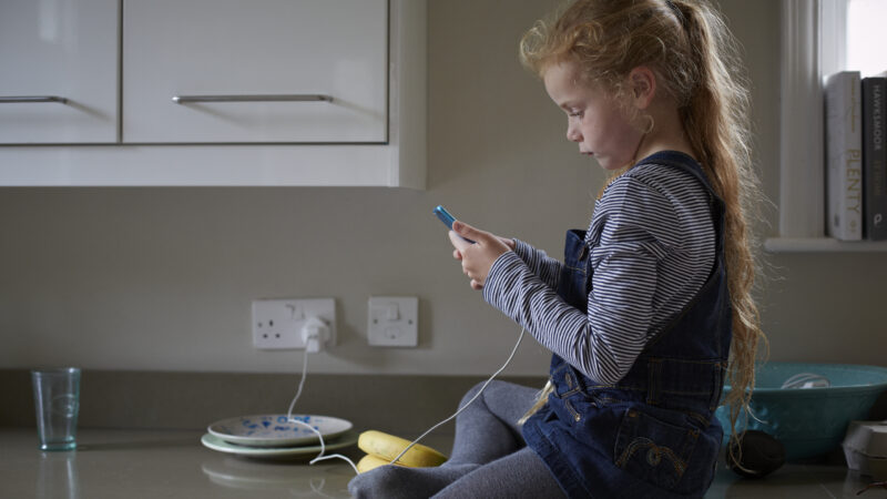 A young girl sat on a kitchen countertop on a phone