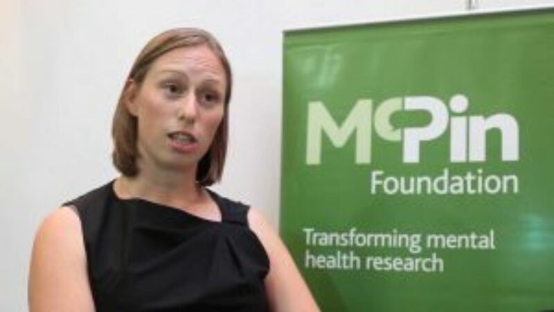 A woman mid-sentence standing in front of a McPin Foundation banner
