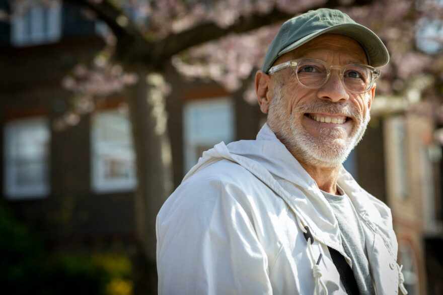 Man wearing a cap and glasses smiling into the camera in front of a tree in blossom
