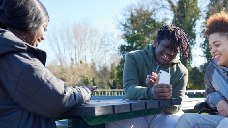 Three young people chatting and smiling looking at phone